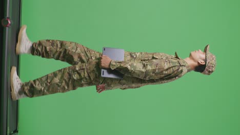 cuerpo lleno de vista lateral hombre asiático soldado sosteniendo una tableta mientras caminaba en el estudio de fondo de la pantalla verde