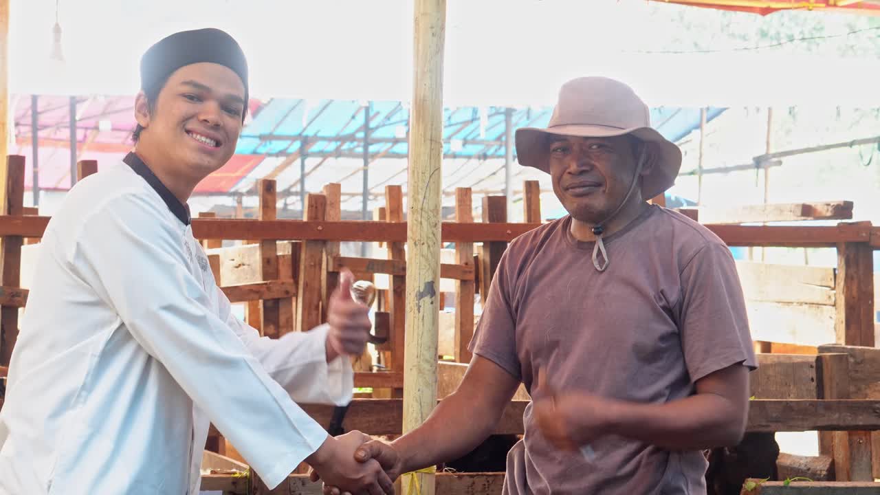 Muslim Man Paying Money and Hand Shaking With Farmer Then Smiling To Camera, Making A Deal For Buying Goat at The Cattle Farm For Islamic and Eid Al Adha Celebration
