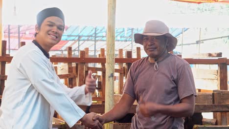 muslim man paying money and hand shaking with farmer then smiling to camera, making a deal for buying goat at the cattle farm for islamic and eid al adha celebration