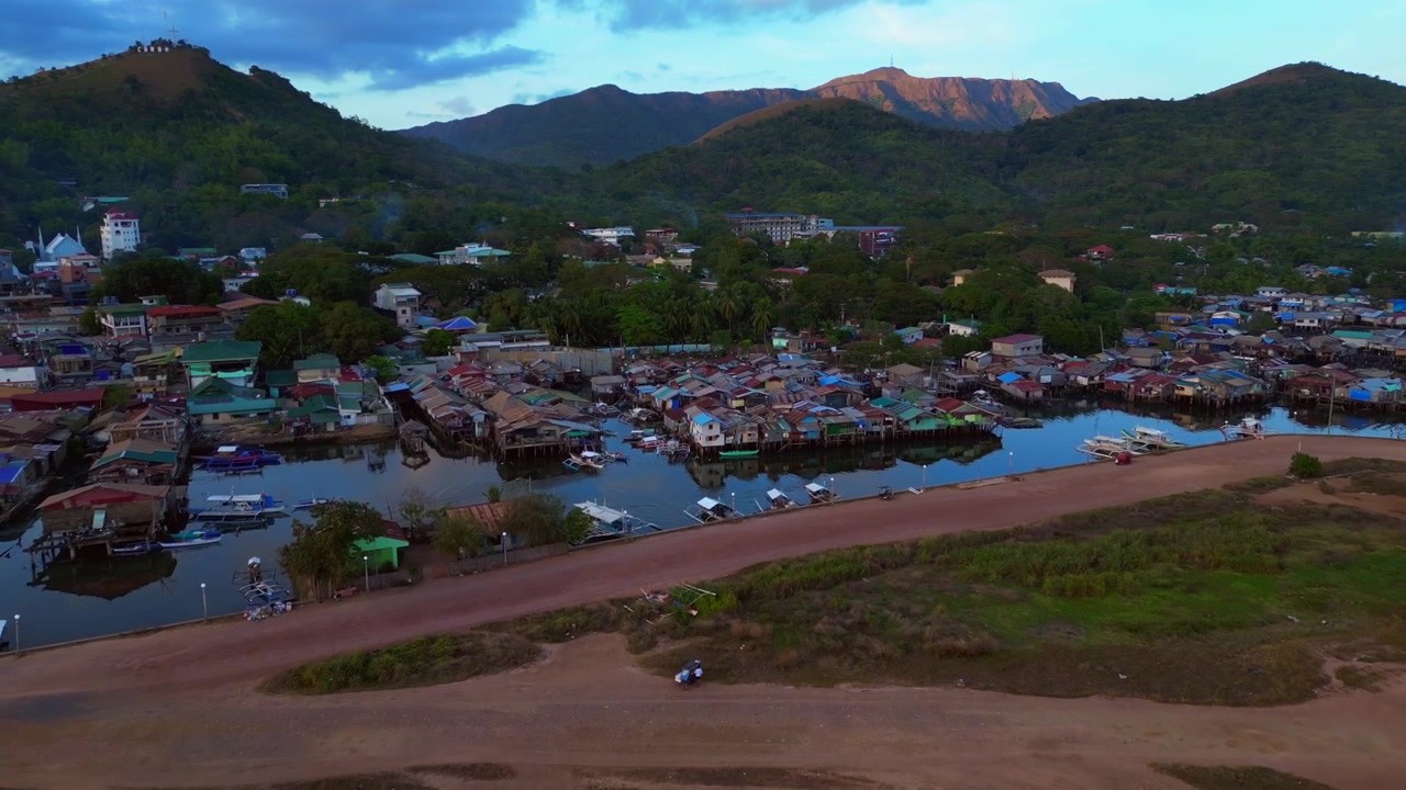 Densas casas flotantes sobre pilotes construidas sobre el agua junto a un muelle, representando comunidad y vida tradicional. Vista aérea mágica, panorama de dron con vuelo inverso