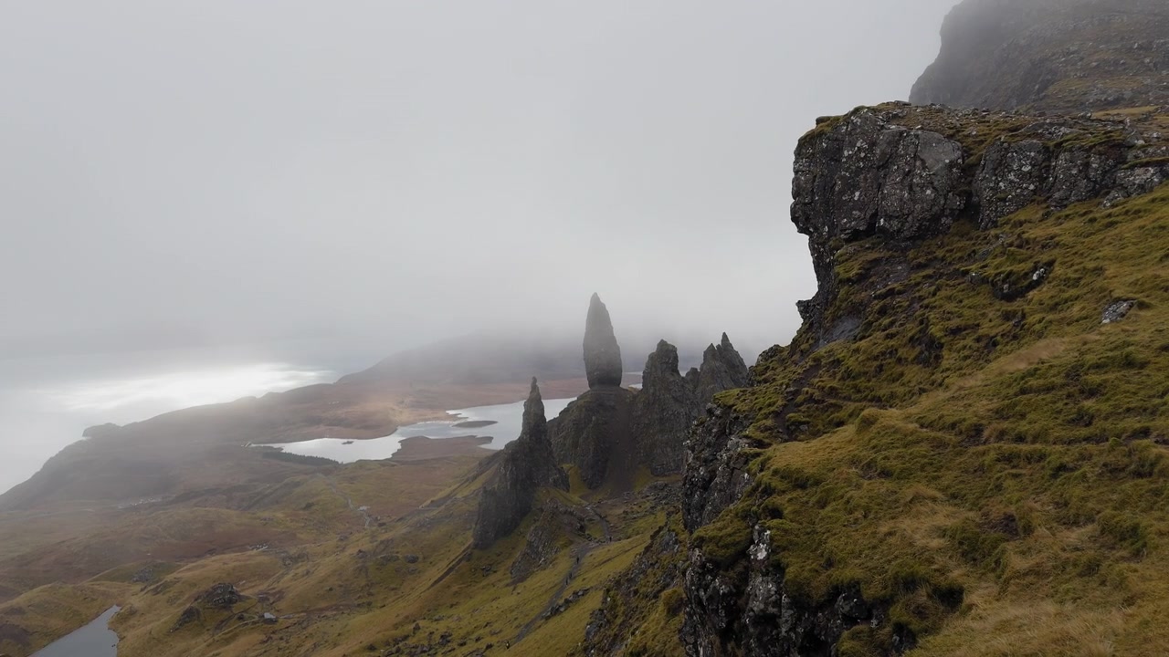 The Storr, Skotsko. Mlhavé pobřežní útesy s oceánskými vlnami tříštícími se dole pod drsnou zelenou krajinou.