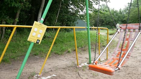 Public-warning-covid-corona-virus-sign-on-park-playground-with-empty-swing-slow-motion