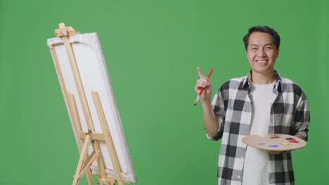 artist with paintbrush and palette in front of easel