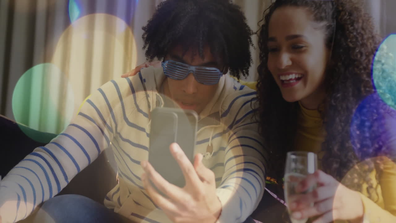 Holding smartphone and smiling, friends with drinks over colorful bokeh animation