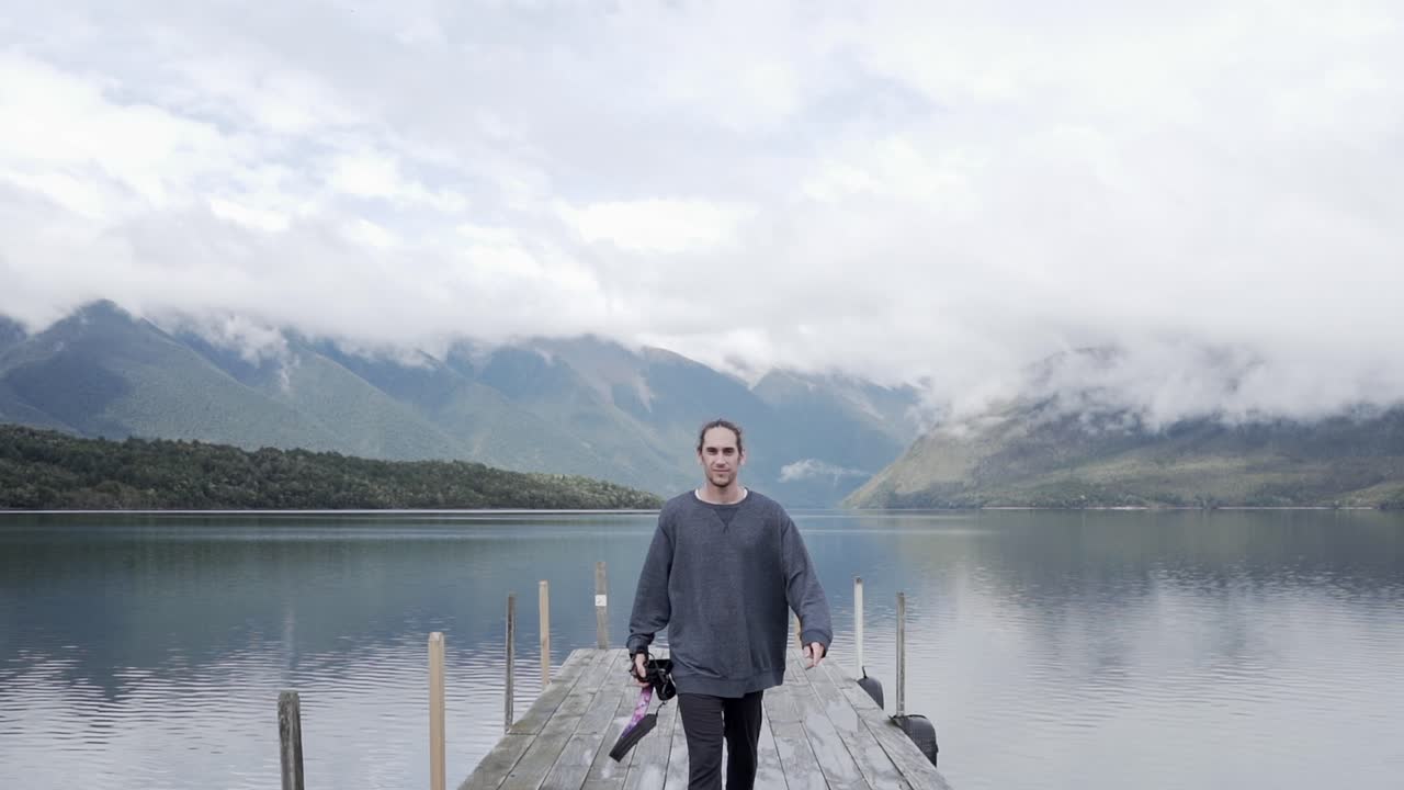 Man walking on pier by a lake with mountains in the background