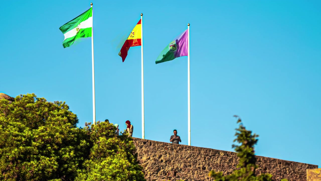 Spain, Malaga and Andalusia flags wave in wind on sunny day, time lapse view