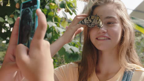 hermosa mariposa en la cara de las niñas con un amigo feliz tomando fotos usando un teléfono inteligente amigos divirtiéndose en el zoológico santuario de vida silvestre compartiendo excursiones en la naturaleza en las redes sociales imágenes 4k