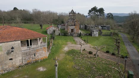 aerial dolly above empty grass field to front of moss covered church, church of santa maria de vilela in punxin ourense spain