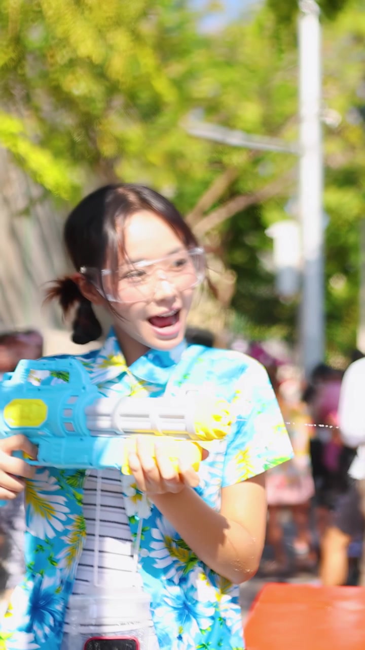 ผู้หญิงไทยร่าเริงสวมเสื้อลายดอกกำลังฉีดปืนฉีดน้ำในช่วงเทศกาลสงกรานต์
