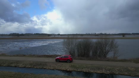 Red-SUV-driving-over-a-sandy-road-next-to-a-river-in-Poland