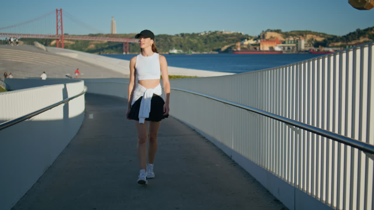 Sporty lady walking urban bridge at serene summer morning. Calm woman strolling
