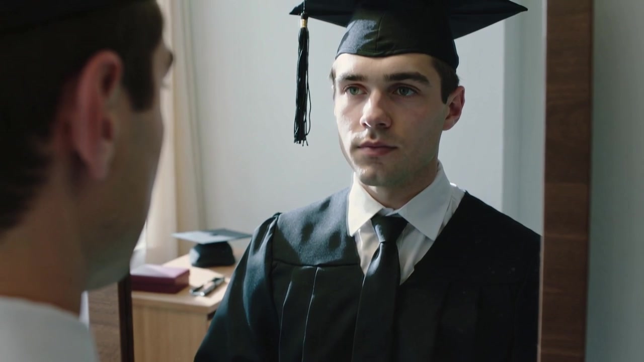 Uomo in toga da laurea che annoda una cravatta scura, sistema il tocco e si guarda allo specchio in camera da letto per la laurea.