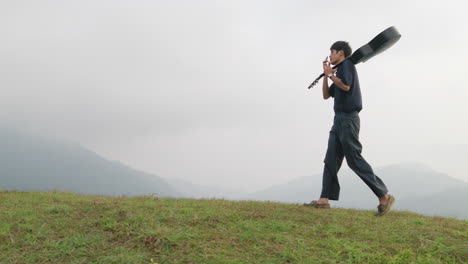 hombre asiático con estilo llevando su guitarra en el hombro en las montañas