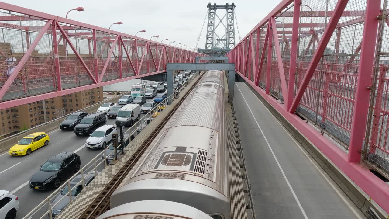 보행자가 위의 자전거를 타고 자동차가 교통 체증을 기다리는 동안 지하철 열차는 뉴욕시의 윌리엄스버그 다리를 통과합니다.