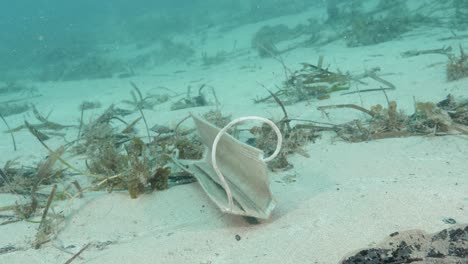 una máscara médica desechada por el brote de covid-19 llega al fondo del océano meciéndose en la corriente con otros desechos y basura marinos.
