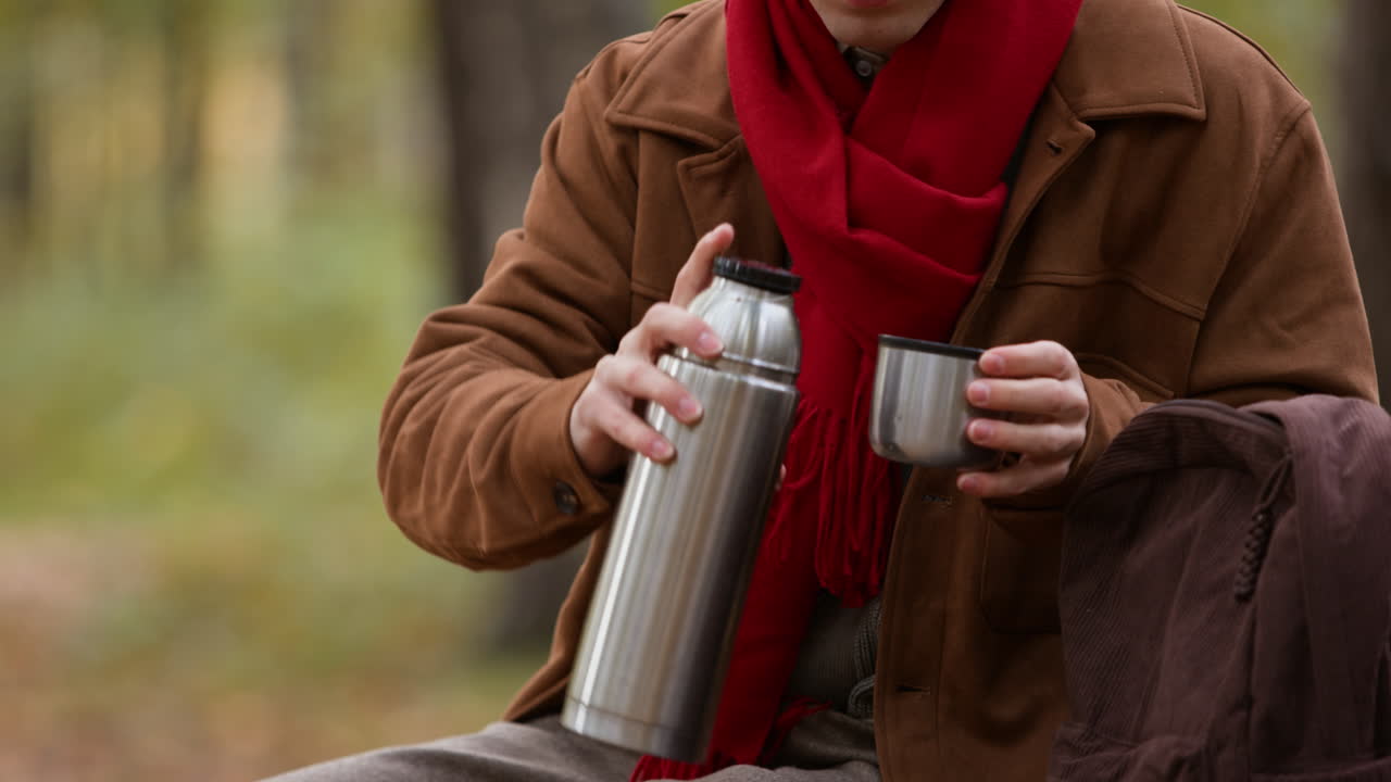 Person pouring drink from thermos into cup outdoors