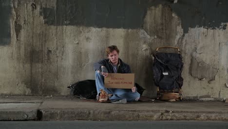 wide shot of a homeless veteran on the sidewalk holding a sign asking for help