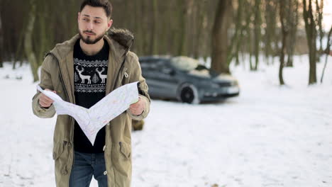 kaukasischer mann, der in einem verschneiten wald auf der karte nach wegbeschreibungen sucht.