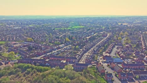 aerial view of wakefield suburban residential area, england, showcasing rows of brick houses, roads, streets, spring greenery, and cars in motion under a clear sky with a distant horizon.