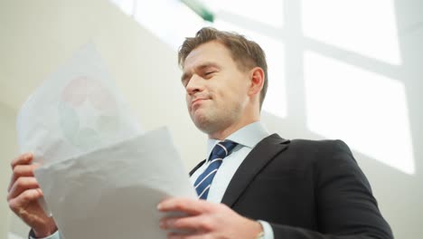 successful manager man holding and examining paper sheet documents in a brightly lit office environment - low angle close-up