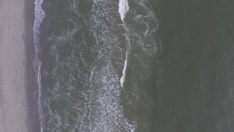 A-topdown-drone-shot-by-the-sea,-during-sunset,-panning-back-and-waves-rolling-in