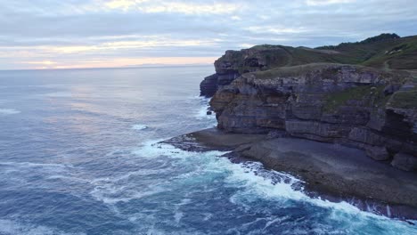 drone capture waves of the blue colored cantabrian sea and island of isla at sunset