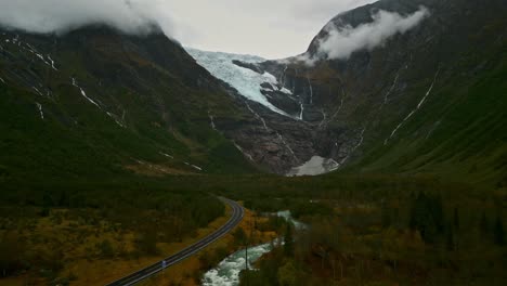 Drone-flies-through-a-valley-over-a-Norwegian-road-towards-a-cloud-covered-Gletcher