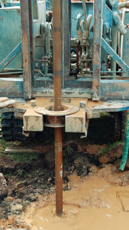 equipment drilling the ground as boring the well. metal pole rotates in the mud. vertical video.