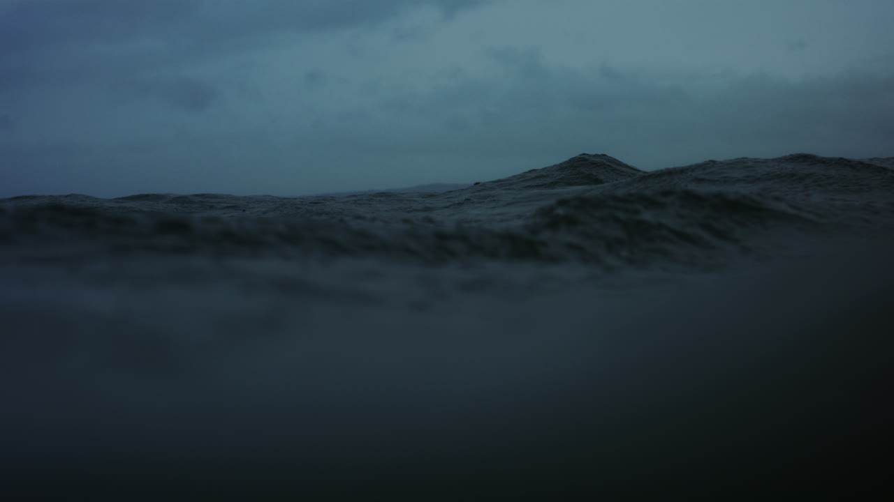 Head bobs in the distance behind ocean wave surface on stormy day in slow motion
