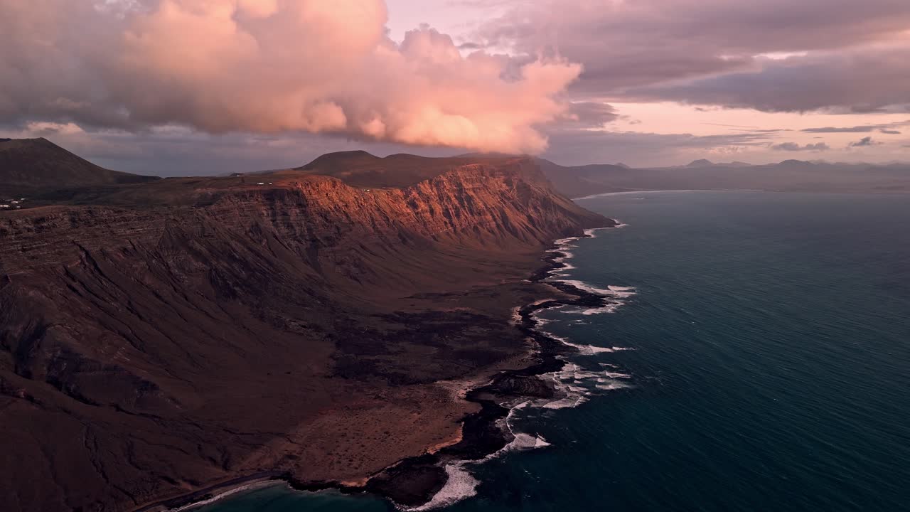 Stunning aerial drone footage of Famara Beach and its dramatic coastal mountains during golden sunset light in Lanzarote, Canary Islands, Spain.