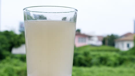 bubbly water in a glass caused by dilution of an antacid or sodium bicarbonate on a backdrop of houses and green vegetation out of focus