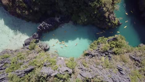 4K-Aerial-top-down-drone-view-of-people-kayaking-in-small-lagoon-on-a-sunny-day-around-Miniloc-Island-in-El-Nido,-Palawan,-Philippines