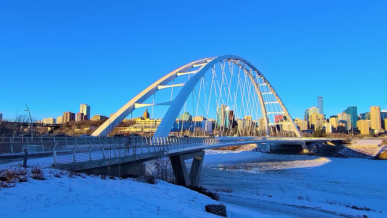 2-2 4k 저속 완벽한 루프 햇살 가득한 겨울 현대식 화이트 월터 데일 다리 교통량과 에드먼턴 시내의 지평선이 있는 북서스캐처원 강을 건너는 두툼한 눈을 건너는 사람들