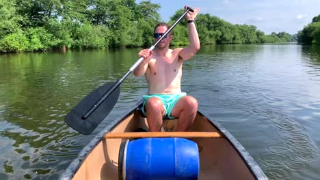 topless man paddles canoe on river wye in sun along green river bank