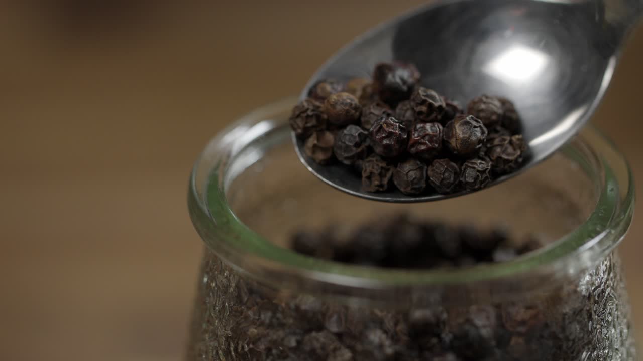 Close up view of whole black pepper in spoon and jar, ingredient for chimichurri sauce