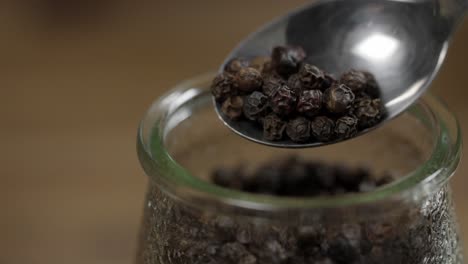 Close-up-view-of-whole-black-pepper-in-spoon-and-jar,-ingredient-for-chimichurri-sauce