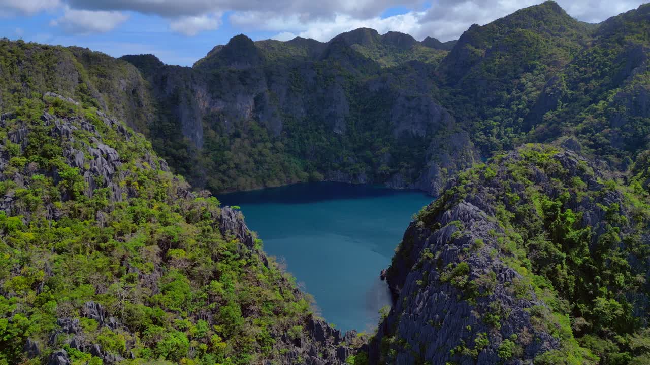 Lago Barracuda na Ilha Coron, Palawan, oferecendo um local de mergulho único. Vegetação verde exuberante cobre altas falésias de calcário que cercam a água azul profunda. Vista aérea deslumbrante, panorama estático pairando.