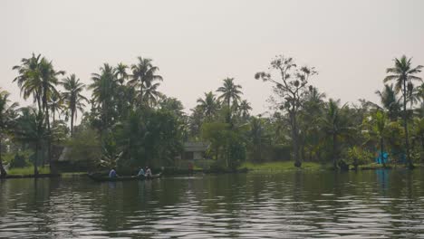 the camera sails by three people in the distance in a small canal boat on the backwaters of kerala with palms on the bank and the midday sun