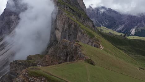 Vuelo-Aéreo-De-Drones-Que-Muestra-A-Una-Pareja-En-El-Borde-Verde-De-La-Montaña-Viendo-La-Majestuosa-Cumbre-De-Las-Montañas-Dolomitas,-Italia