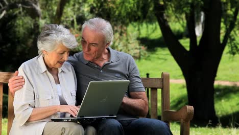 un hombre y una mujer mayores mirando una computadora portátil sentados en un banco