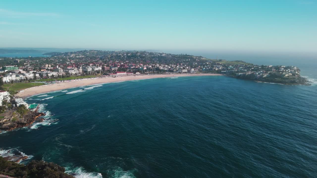 amplias imágenes aéreas de drones que muestran la playa de bondi, su costa dorada y el suburbio costero circundante bajo cielos azules claros. capturada en 4k a 25 fps, la escena destaca la icónica costa de sídney.