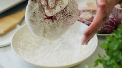 woman rolling veal shank in flour before frying