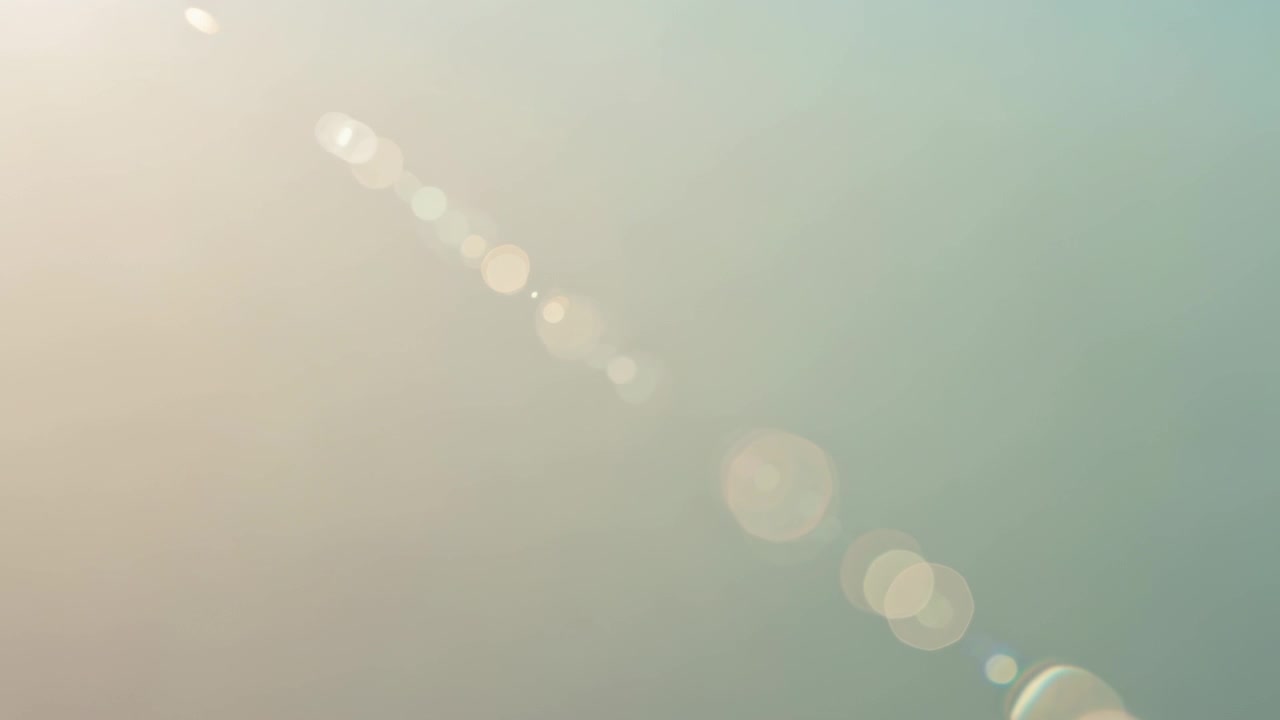 太陽光がカメラレンズに当たり、斜めのレンズフレアが発生。ピーチ色からティール色へと移り変わる空を背景に。