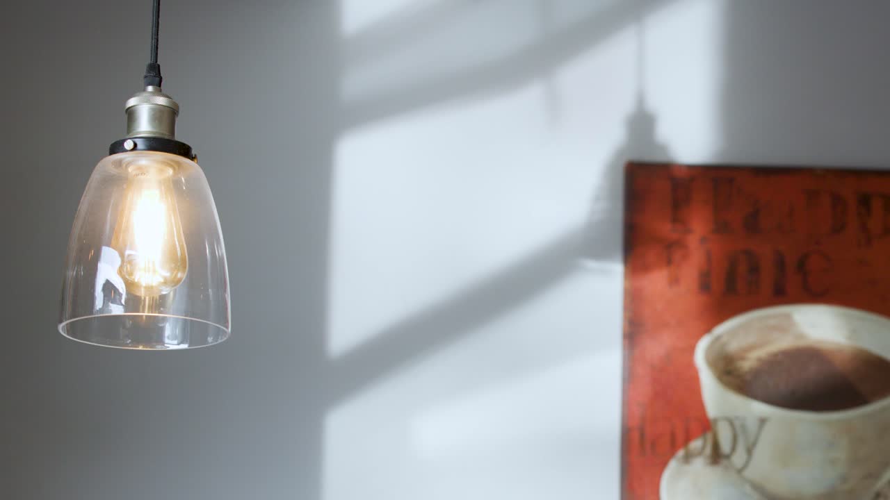 Pendant light and coffee painting illuminated by sunlight, casting dynamic shadows on cafe wall