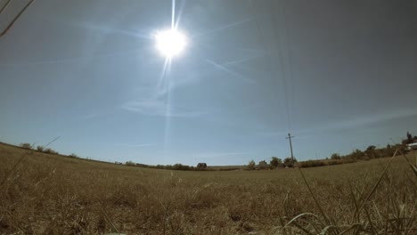 Zeitraffer---Sonne-Bewegt-Sich-über-Den-Himmel-über-Ein-Feld-Mit-Ein-Paar-Objekten,-Die-Am-Himmel-Fliegen-Und-Wolkenspuren-Verursachen