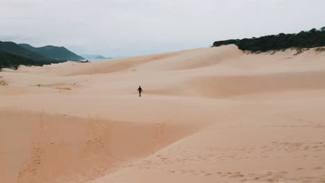 Sandboarder-walking-on-sand-dunes-near-the-tropical-beach-of-Garopaba,-Santa-Catarina,-Brazil