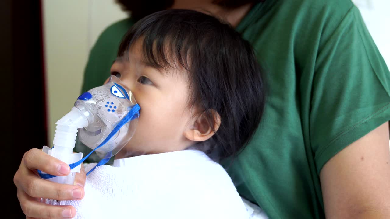 Bambina asiatica in terapia respiratoria accudita dalla madre.
