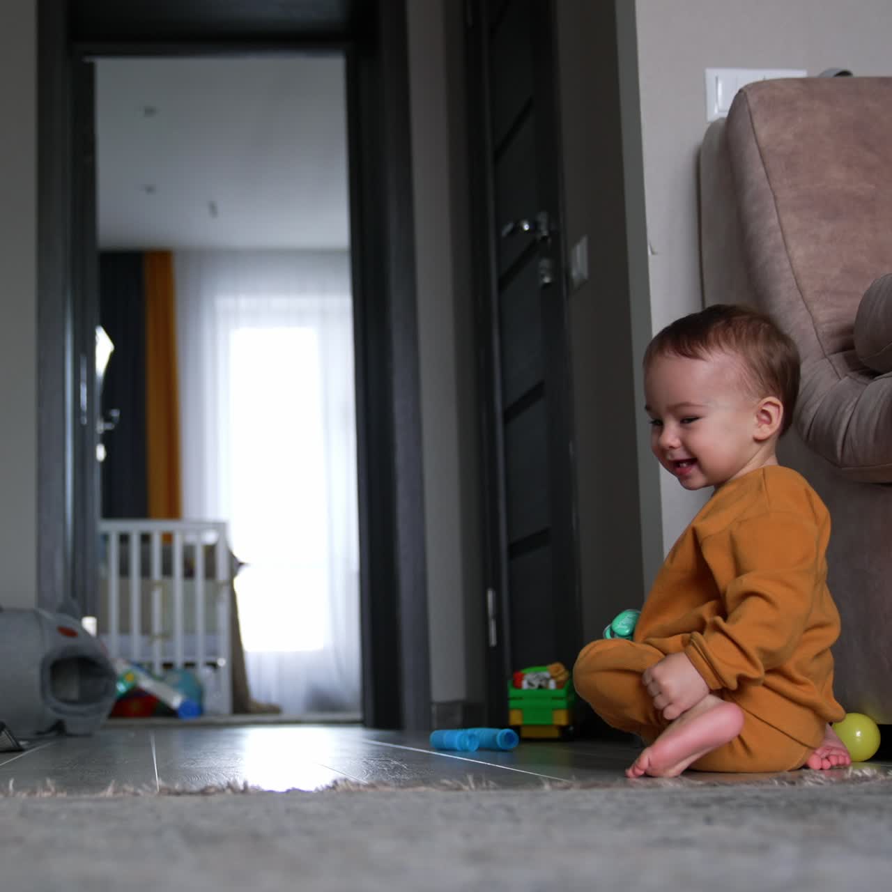 Little barefoot kid plays with a ball on the floor of the room. Adorable child smiling sweetly chasing the toy
