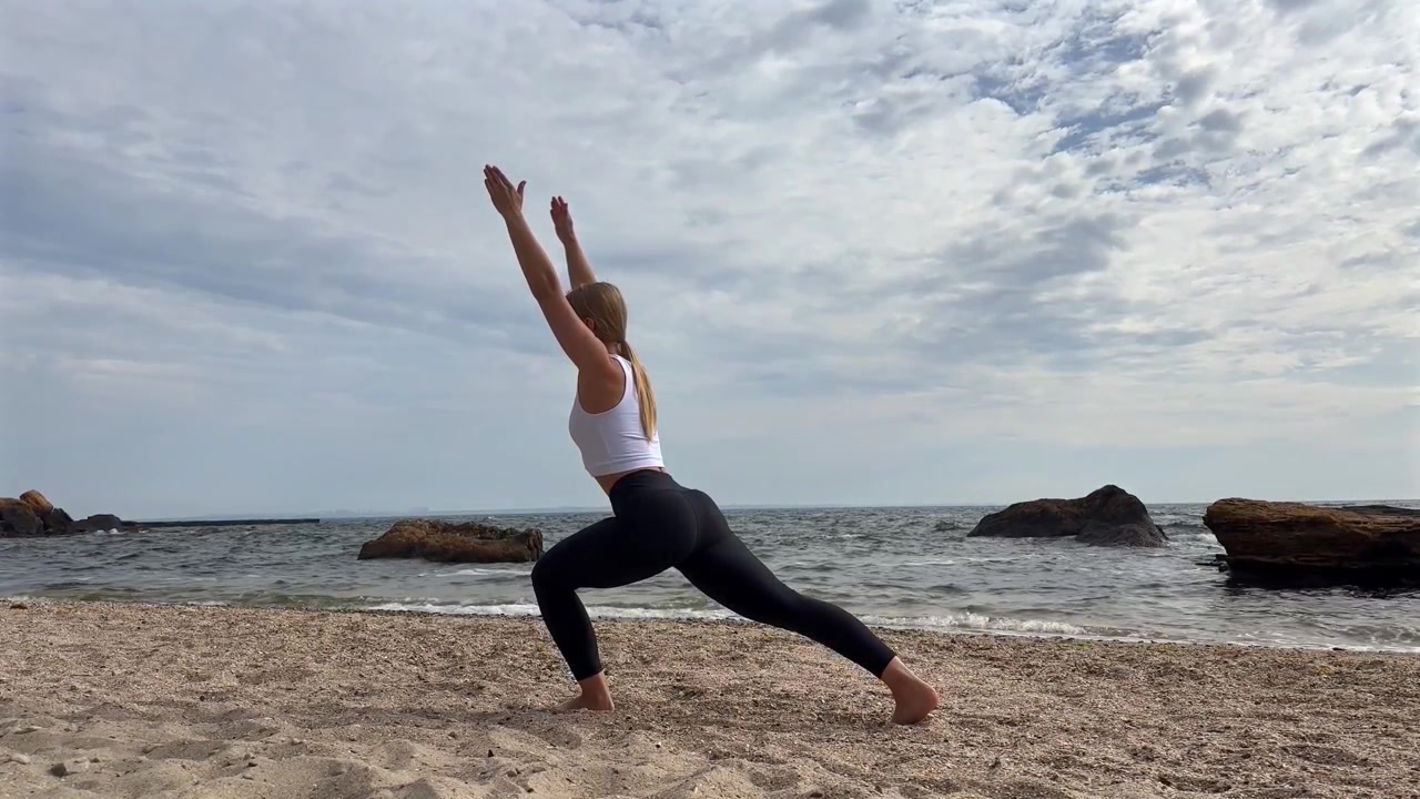 Giovane donna che pratica la posizione yoga dell'affondo sulla spiaggia