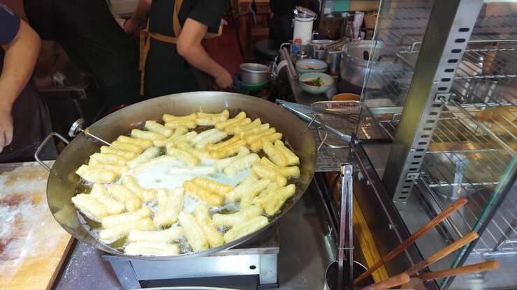 Close-up shot of golden dough sticks bubbling in a large wok at a market.